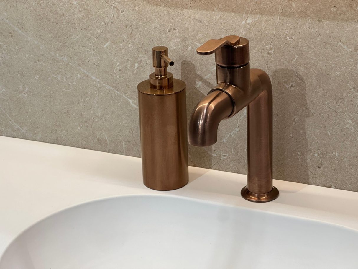 Grifo y dispensador de jabonar de acabado bronce en una encimera de baño.