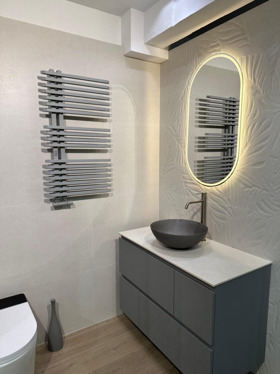 Baño moderno con lavabo circular, espejo iluminado y toallero de diseño.